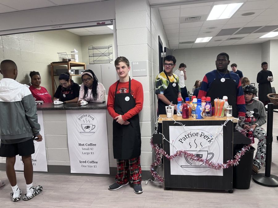 Sophomore Jackson Treadwell (center) tells passer-bys Merry Christmas as they grab a coffee from the Patriot Perk counter where  Tori Nichols (left) and Tara Richardson (center left) cashier. Bryce Phan (center right) and Devin Davis (right) man the coffee add-ins. (Photo by Luke McLendon)