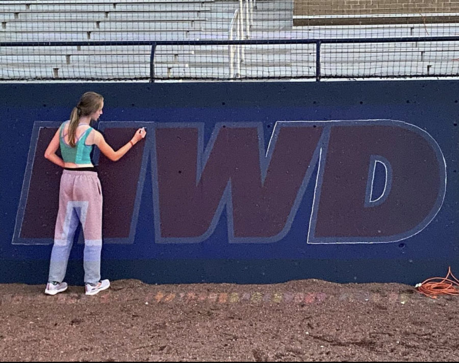 Chandler Binkley traces the outline of her mural for the baseball team. Photo contributed by Chandler Binkley. 