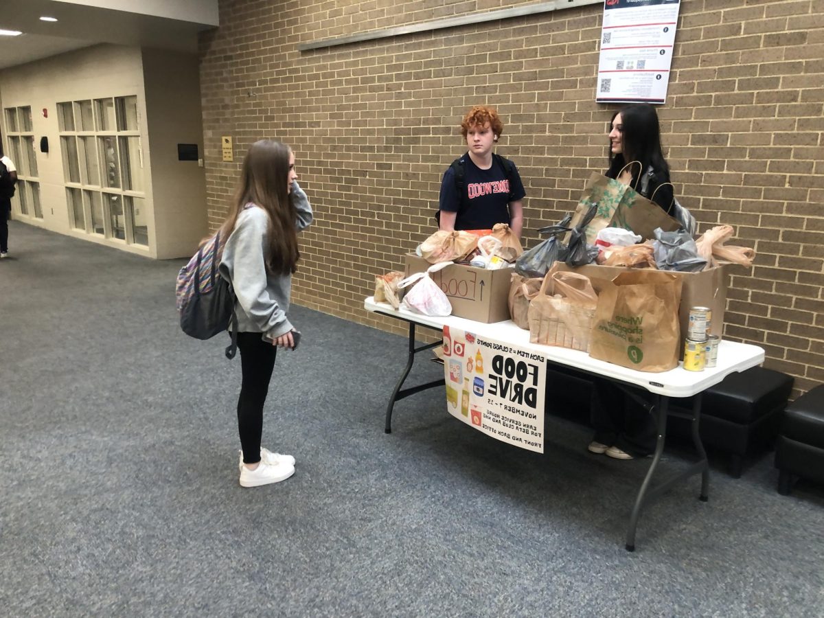 HHS student conversing with Thanksgiving Food Drive workers after donating canned goods.