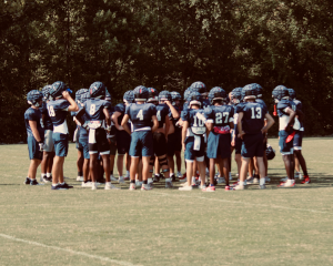 Varsity football players enter a huddle during practice. Head coach Ben Burgeson credits his faith in the team to their collaboration on and off the field.