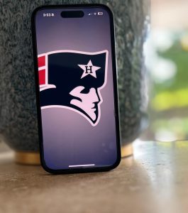 An iPhone displays the Homewood Athletics logo. The app features scores, rosters and news all in one place.